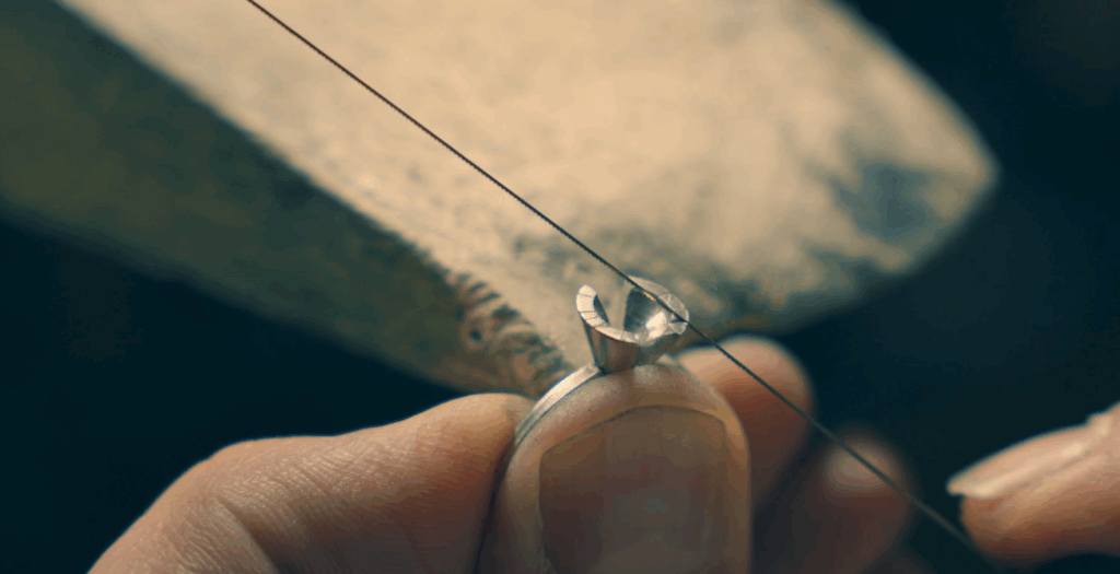 Close-up of a master jeweller shaping a handmade ring from solid metal using a fine saw in a traditional Melbourne workshop.