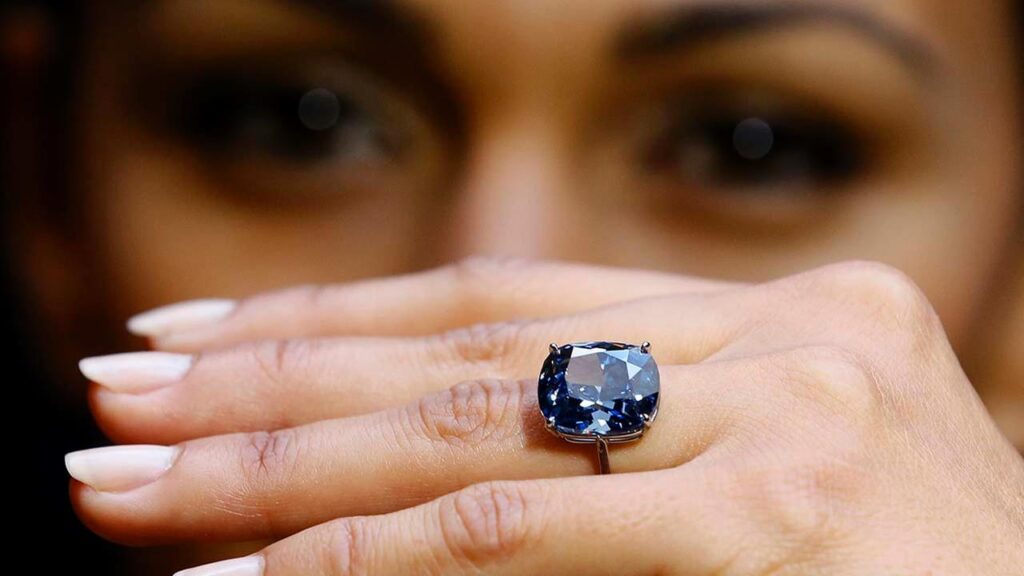 dark blue diamond set into a ring, blue moon of josephine blue diamond, held up to someones face for scale.