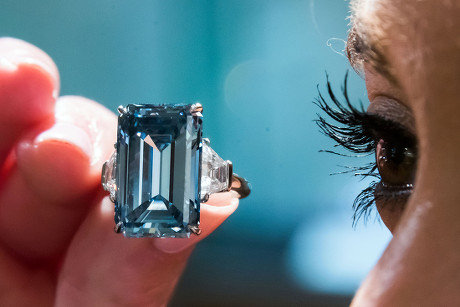 a rare blue diamond, set into a ring, held up to the eye of a person- to show the scale of largeness.
