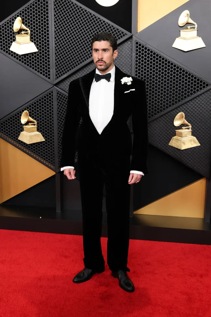 BAD Bunny, standing on the 2026 grammys red carpet wearing a black suit and bowtie
