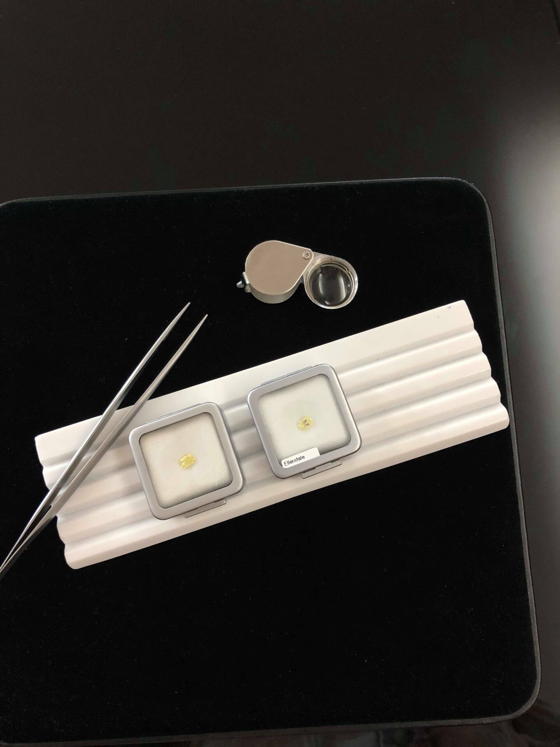 two packaged natural yellow diamonds ready to be inspected sitting with tweezers and a eye glass