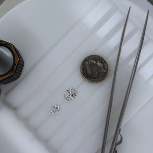 Top-down view of a 1 carat and 2 carat round brilliant cut diamond displayed on a white jeweller’s tray, positioned beside an Australian 5 cent coin and precision tweezers for size comparison.