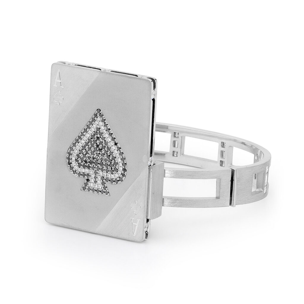 A cuff bracelet in platinum, designed to replicate an ace up the sleeve, set with white diamonds, black diamond and treated blue diamonds to replicate a ace card from a deck of cards