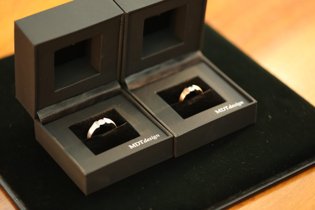 Two engagement rings displayed side by side in MDT Design boxes, representing matching same-sex engagement rings.
