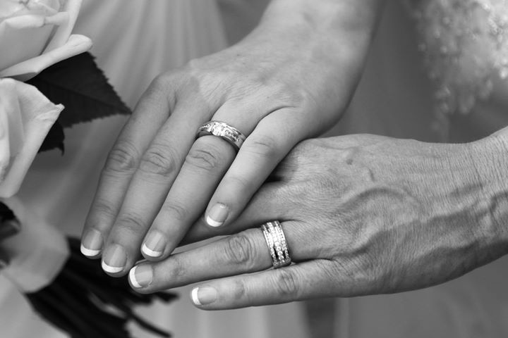 Two hands wearing diamond wedding bands symbolising same-sex marriage and commitment.