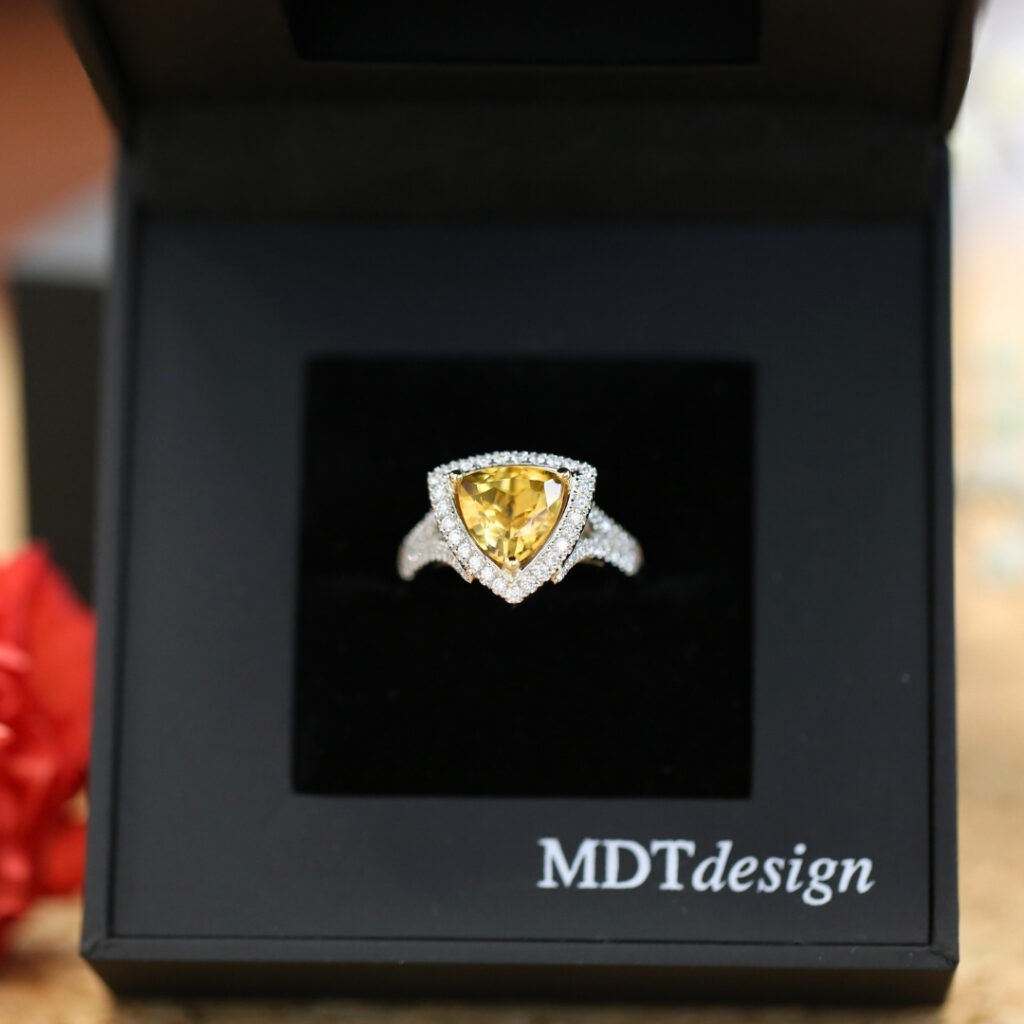 orange sapphire triangle trilliant with a halo of white diamonds around it in a cocktail ring