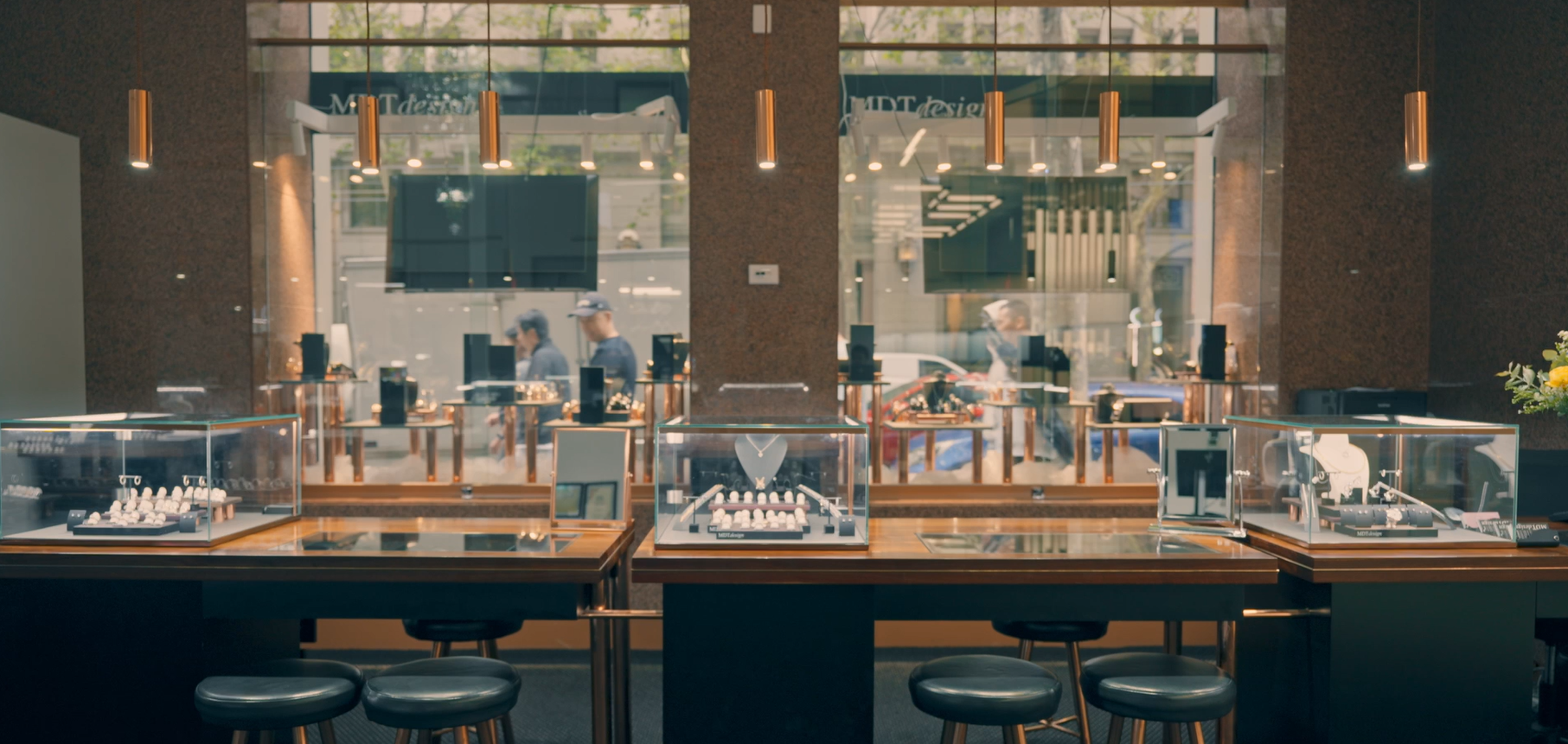 Interior of Melbourne jewellery boutique MDT DESIGN with glass display cases showcasing custom handmade engagement rings and necklaces, warm lighting, and a view through the front windows onto Collins street outside.