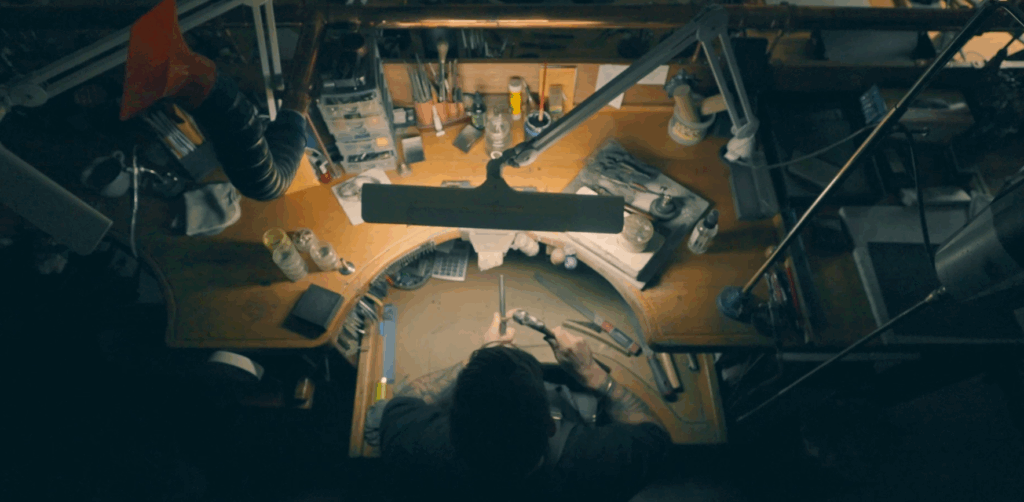 Overhead view of a jeweller hand forging metal at a traditional workbench in a Melbourne workshop, surrounded by tools, illustrating the handmade jewellery process.