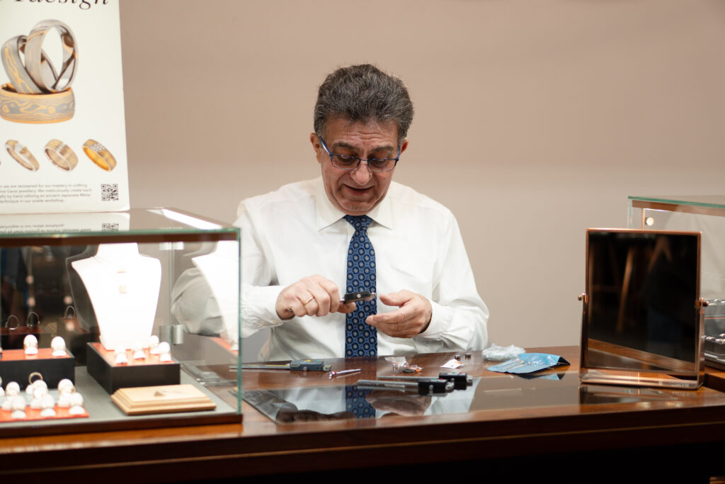 Nicholas Theochari working with jewellery at the MDT DESIGN Melbourne boutique, surrounded by handmade pieces and jeweller’s tools.