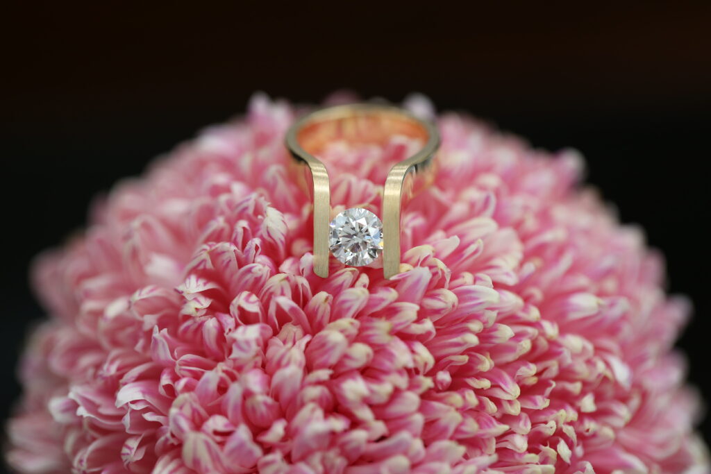 Yellow gold tension set ring with a round brilliant diamond suspended between the open sides of the band.
