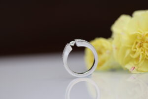 White gold tension set diamond ring with a diamond-set band, photographed beside yellow flowers.